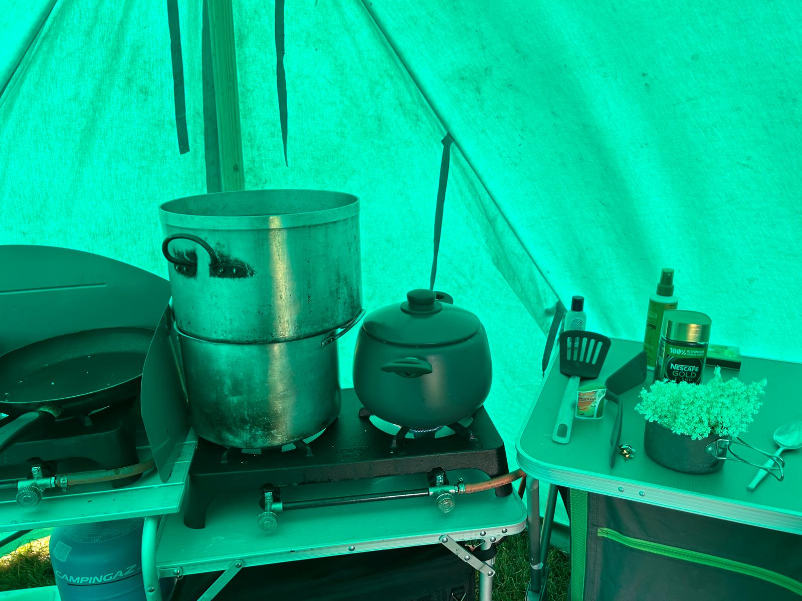 Camp cooking setup inside a green tent with pots on a gas stove